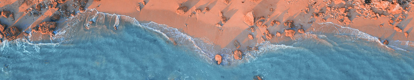 Aerial view of waves meeting a sandy shoreline with scattered rocks along the coast.