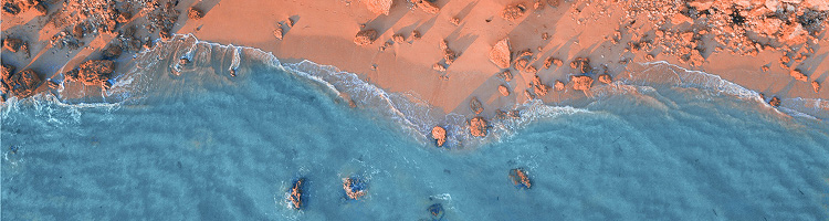 Aerial view of waves meeting a sandy shoreline with scattered rocks along the coast.