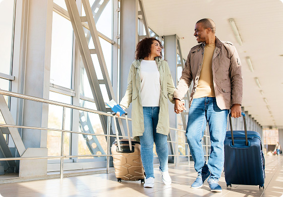 Two people walk through an airport terminal while pulling rolling suitcases.