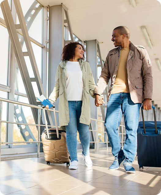 Two people walk through an airport terminal while pulling rolling suitcases.